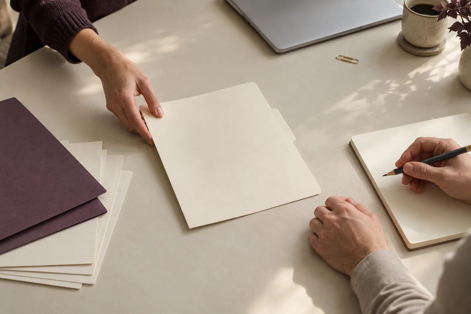 Sur une table de travail, des mains isolent un dossier parmi des documents pour le cadrer ensemble.